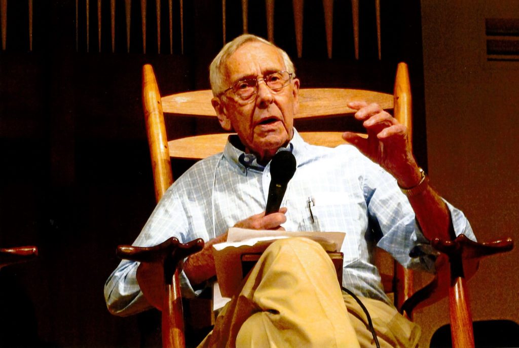 man speaking to a crowd while sitting in a rocking chair