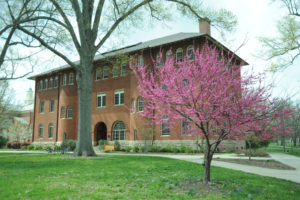 Angled view of a three story brown brick building with two trees.