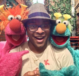 Alumnus Hayes poses with two Sesame Street characters