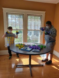 Student and child wearing masks and gloves while cleaning and filling Easter eggs with candy.