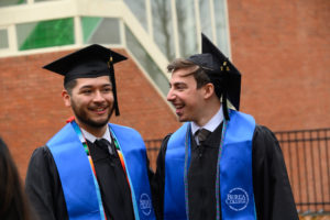 Two men posing in their caps and gowns and laughing