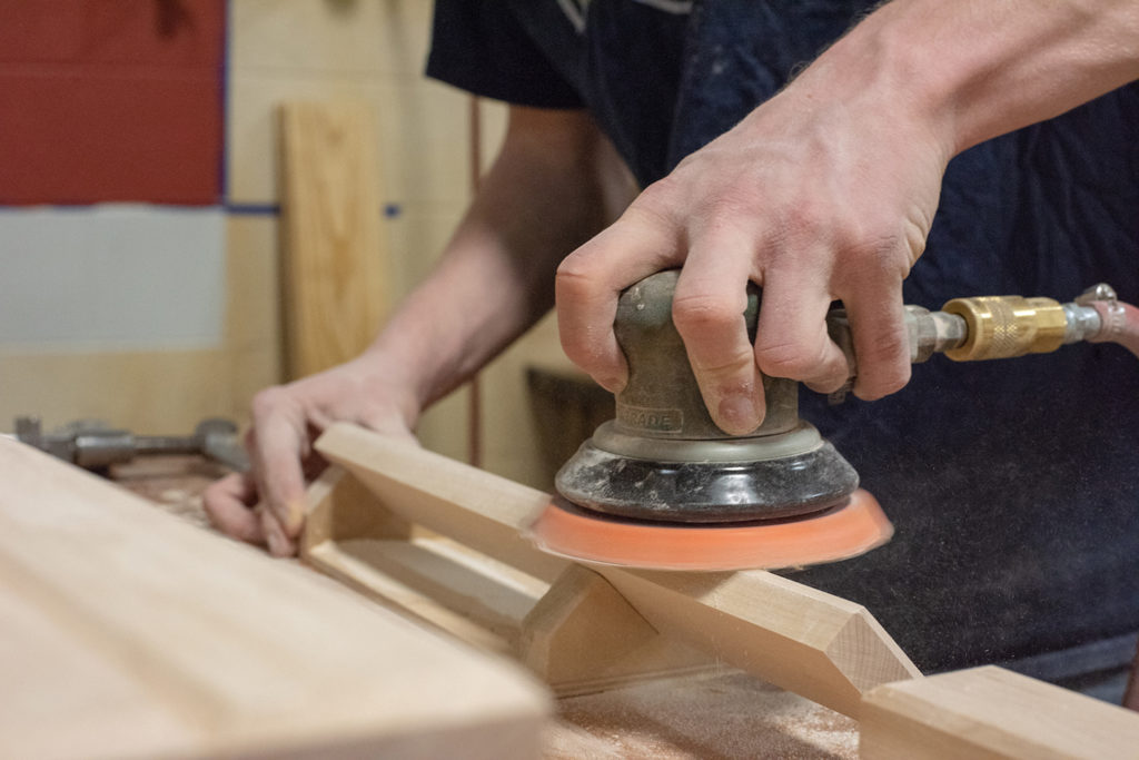 Person using a sander to create a bevel on a plank of wood